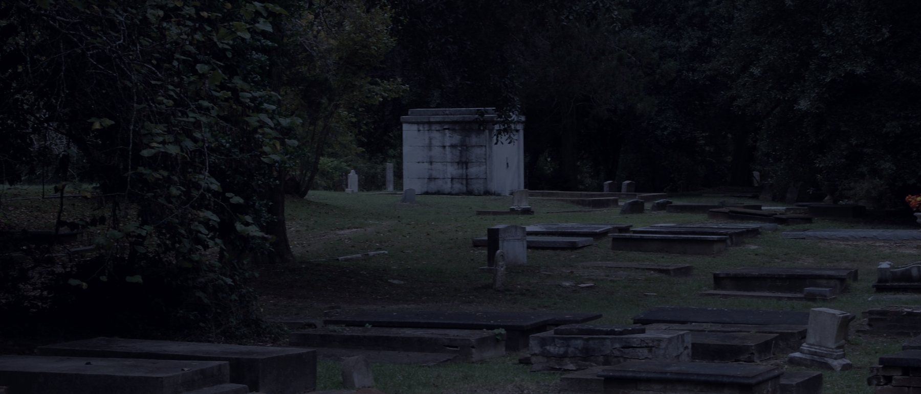 Table tombs and a single white mausoleum under heavy oaks in the American Cemetery
